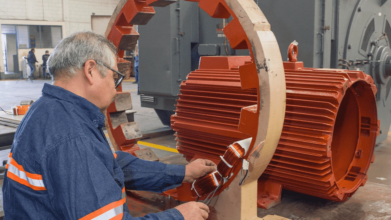 Técnico especialista de SIMSA realizando el embobinado manual de un motor eléctrico industrial en taller de reparaciones.